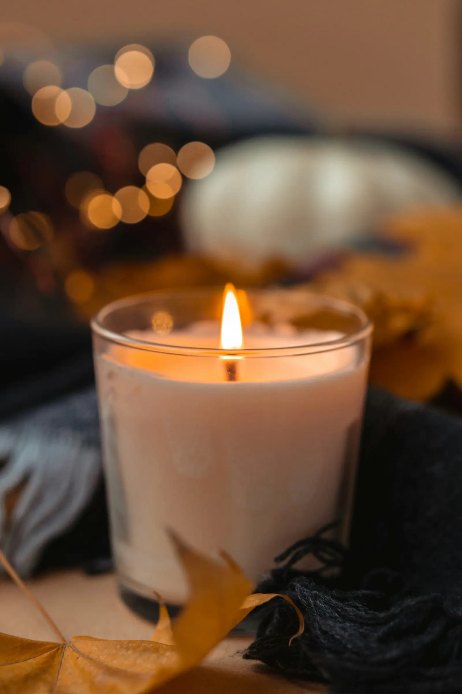 A glowing glass candle styled with warm textiles and autumn leaves